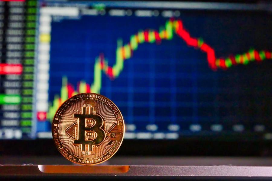 Jeton bitcoin physique devant un écran de trading.