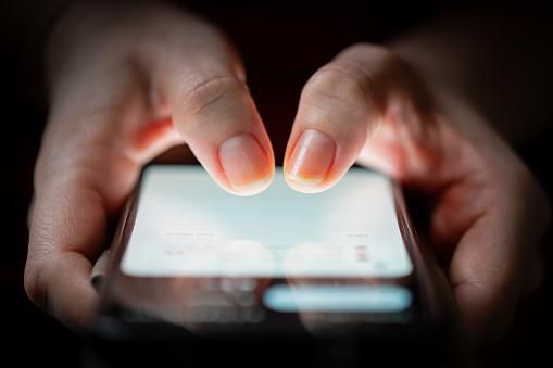 Gros plan sur les pouces de deux femmes touchant un écran de smartphone dans l'obscurité.