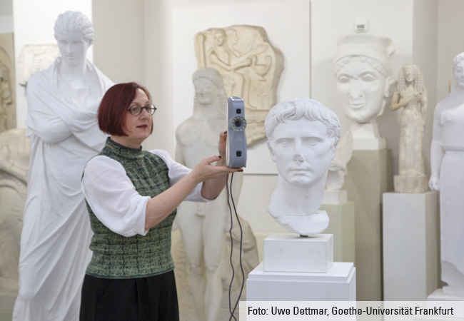 Dr. Ulrike Wolf avec le scanner à lumière à bande devant une sculpture.