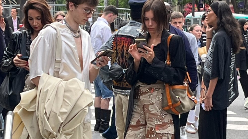 Un groupe de personnes stylées se tient sur une rue, utilisant leur smartphone.